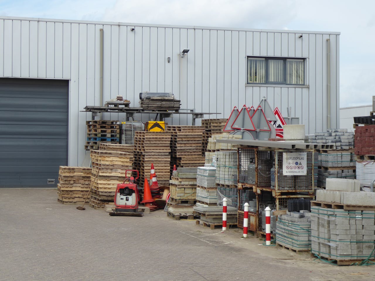 why-choose-us An outdoor yard with stacked construction supplies and pallets against a warehouse.