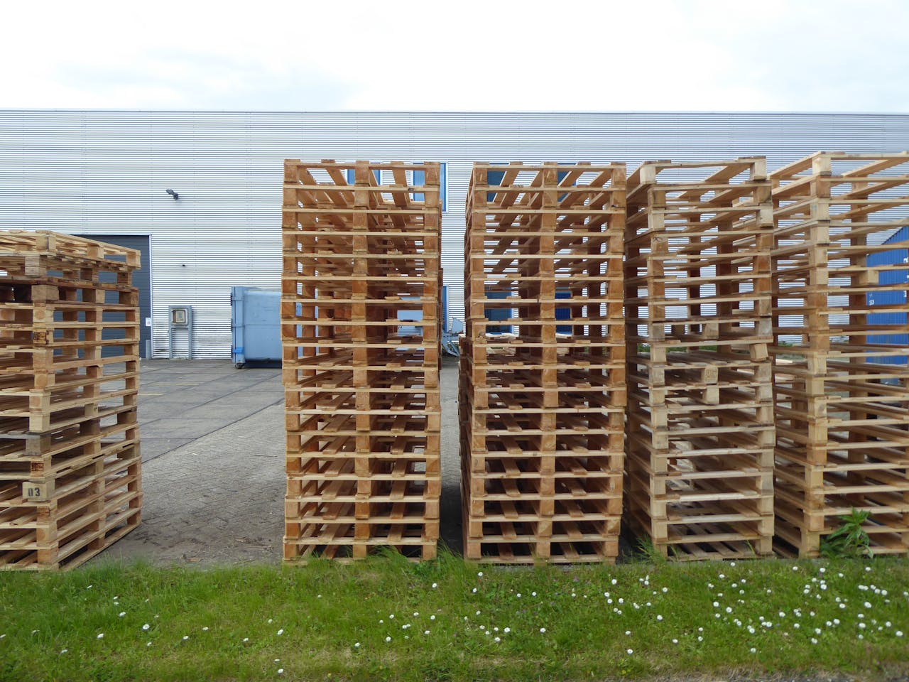 ours-journey Rows of wooden pallets stacked outdoors near a warehouse, perfect for industrial and logistics themes.