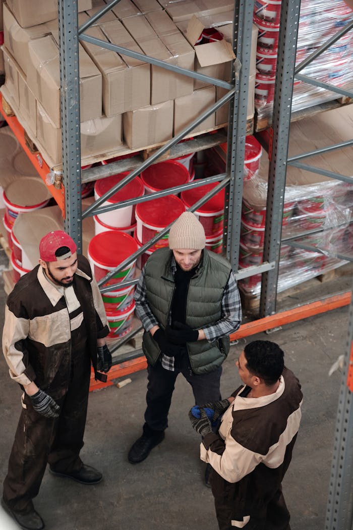 about-img Group of warehouse workers discussing logistics in an industrial storage area with shelves and packaging.
