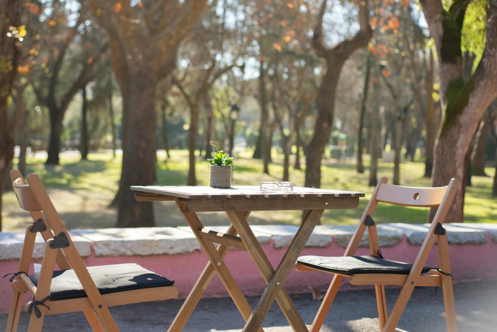 Wooden table and chairs set in a tranquil park setting under bright daylight.