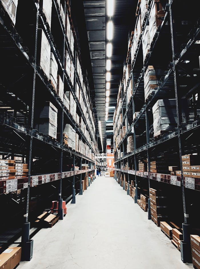 about-02 A wide aisle in a large warehouse filled with stacked boxes on high shelves.